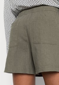 Oliivinvihreät shortsit, jotka on valmistettu kevyestä kankaasta. Niissä on joustava vyötärönauha, kaksi takataskua ja suora helma.