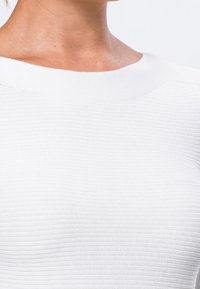 Top bianco in maglia con un motivo a coste testurizzato, caratterizzato da un ampio scollo e un design aderente, che enfatizza una finitura liscia.