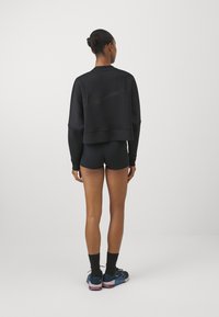 Black cropped sweatshirt with long sleeves, featuring a subtle Nike logo on the back. Paired with black shorts and blue athletic shoes.