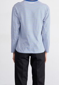 Långärmad skjorta med blå och vita horisontella ränder, rund halsringning med blå kant, i bomullsmaterial, avslappnad passform, ihopparad med svarta byxor.