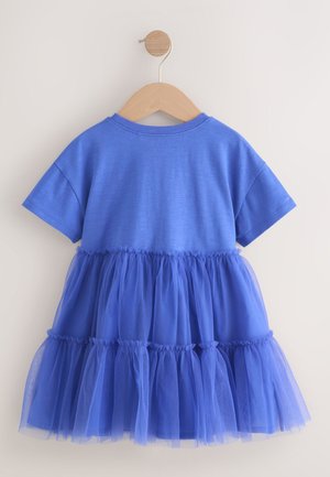 Robe bleue à manches courtes avec une jupe en tulle superposée, suspendue sur un cintre en bois devant un mur clair uni.