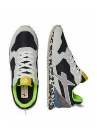 Sneakers bianco e nero con una tomaia in tessuto testurizzato, interno verde brillante e suola decorata con accenti grigi, neri e bianchi.