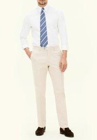 Chinos beige con vestibilità dritta, dotati di chiusura a bottone e passanti per cintura, abbinati a una camicia bianca con bottoni e a una cravatta a righe blu.