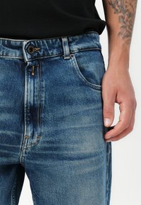 Blue denim jeans featuring a classic straight leg design, with subtle fading and contrast stitching. Standard five-pocket styling.