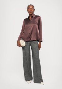 Saténová košile na knoflíky v tlumené mauve barvě, spárovaná s šedými širokými kalhotami. Tento outfit doplňuje minimalistická kabelka a bílé špičaté boty.