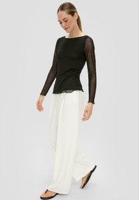 Czarny długi rękaw bluzka z przezroczystymi rękawami i falbaniastym dołem, połączona z białymi szerokimi spodniami i czarnymi klapkami. Gładka struktura materiału.