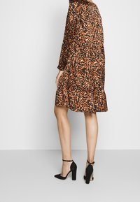 Leopardmönstrad klänning i orange och svart tyg, med långa ärmar och volangkant, matchad med svarta högklackade skor.