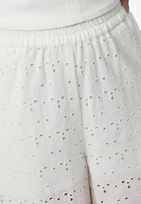 Shorts en coton blanc avec des découpes florales brodées, dotés d'une taille élastique et d'une texture douce.