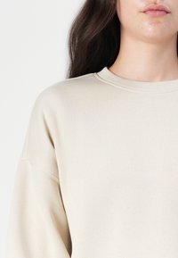 Beige hettegenser med rund hals, ribbestrikkede mansjetter og en myk tekstur, med avslappet passform og droppede skuldre for komfort.