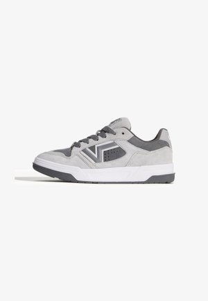 Grå og hvid lav-toppet sneaker med sorte snørebånd og et V-formet design på siden, sat mod en hvid baggrund.