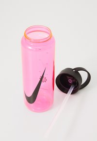 Roze kunststof waterfles met meetstreepjes, zwart Nike swoosh-logo en een zwarte dop met een drinkrietje en handvat.