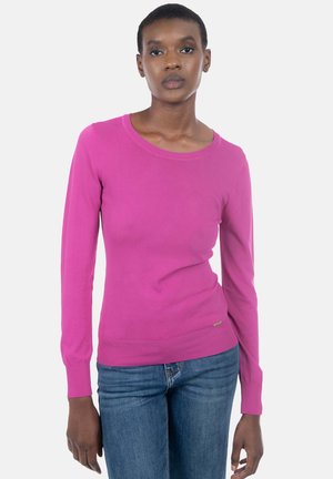 Strak aangesloten trui met lange mouwen in felroze gebreide stof, met een ronde halslijn en geribbelde manchetten, gecombineerd met blauwe spijkerbroek.