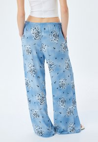 Pantalon large bleu clair en tissu doux, avec un motif paisley complexe noir et blanc et des poches latérales. Taille élastique.
