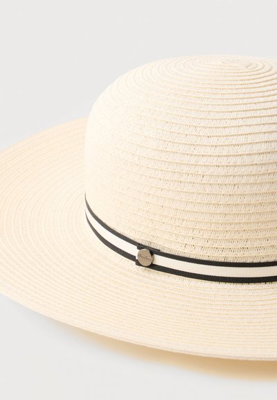Ευρύγεια μπεζ πλεκτό καπέλο ηλίου με μαύρη και λευκή ριγέ ταινία και μικρή στρογγυλή μεταλλική λεπτομέρεια λογότυπου.