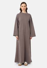 Robe longue et ample en tissu gris doux. Présente des manches larges, un col rond et descend jusqu'aux chevilles. Associée à des baskets blanches.