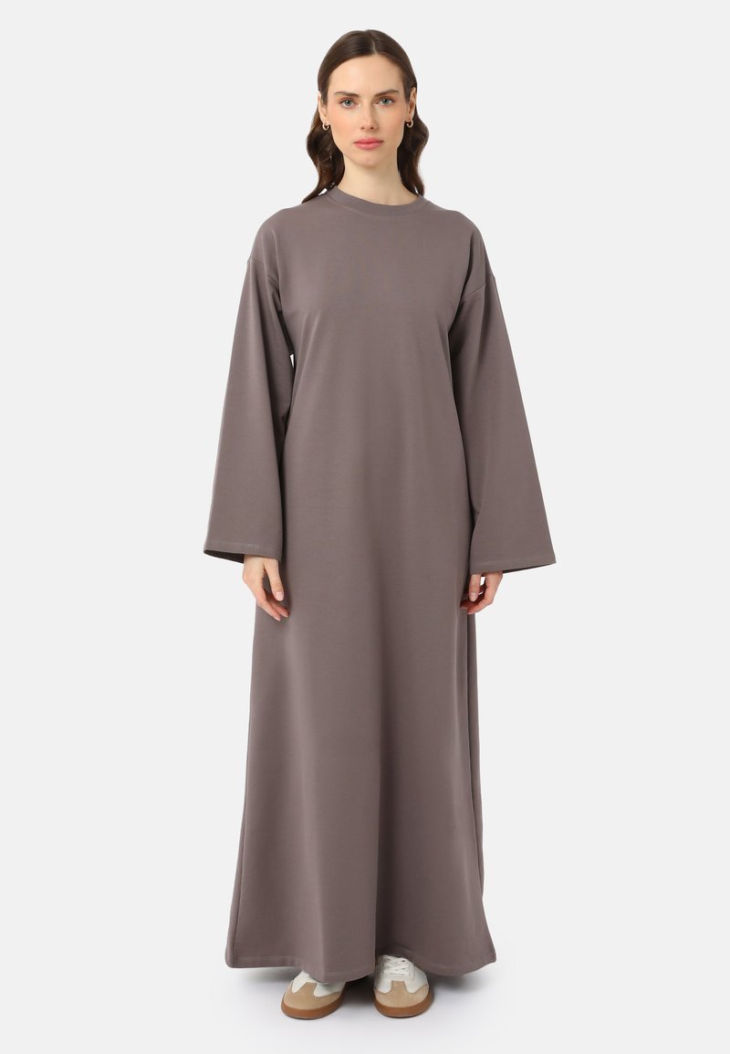 Robe longue et ample en tissu gris doux. Présente des manches larges, un col rond et descend jusqu'aux chevilles. Associée à des baskets blanches.