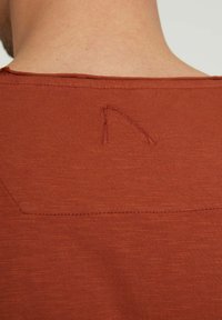 Rudų oranžinės spalvos marškinėliai su minkšta tekstūra, su subtiliu siūtu trikampio formos akcentu nugaroje ir apvaliu kaklu.