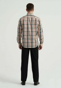 Chemise à carreaux rouge et noir à manches longues avec détails de boutons, associée à un pantalon et des chaussures noirs, vue de dos contre un fond neutre.