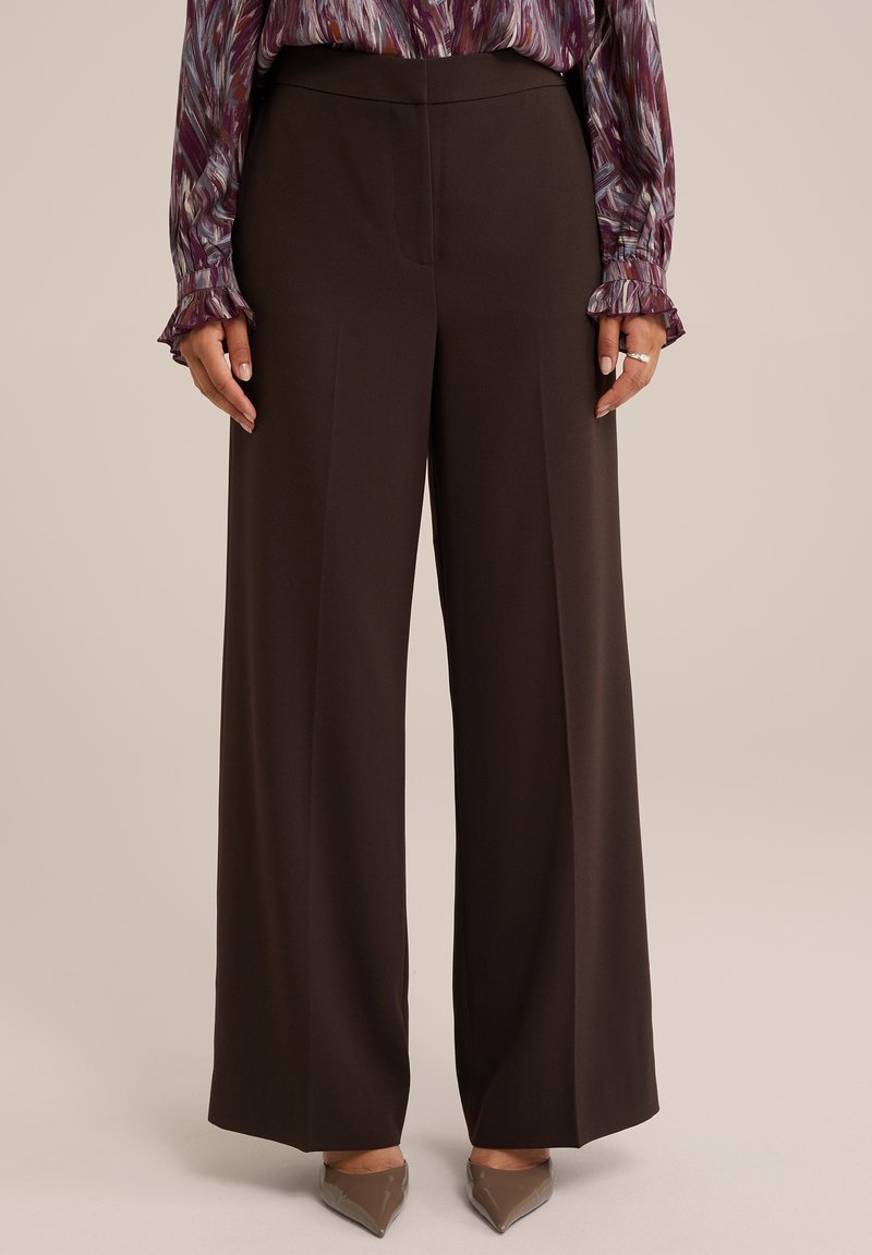 Woman wearing high-waisted, wide-leg dark brown pants, paired with taupe pointed-toe heels and a long-sleeve patterned blouse.