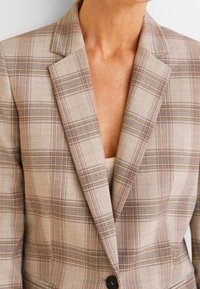 Kostkovaný blazer v béžové, tan a hnědé barvě s klopovým límcem, jednobuttonovým zapínáním a texturovanou tkaninou. Detailní pohled, viditelné krátké rukávy.