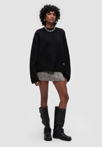 Czarny, oversize sweter wykonany z dzianiny o teksturowanym wykończeniu, z wysokim kołnierzem, w połączeniu z mini spódnicą w wzór houndstooth i czarnymi skórzanymi butami za kolano.