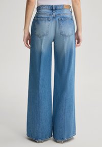 Jasnoniebieskie dżinsy typu wide-leg z wysokim stanem, pięcioma kieszeniami i skórzaną metką marki z tyłu. Materiał ma teksturowane wykończenie dżinsu.