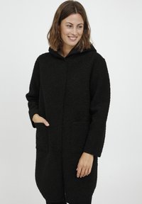 Fekete, kapucnis kabát, texturált anyagból, puha, bolyhos megjelenéssel. Két elülső zsebe és gombos záródása van.