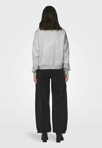 Szürke, túlságosan nagy pulóver esésvállal, amelyet rövid derekú, fekete, bő nadrággal párosítanak, amely zsebekkel és egyenes szárú szabással rendelkezik.