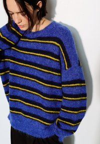 Pull rayé bleu en matériau duveteux, avec des rayures horizontales bleu foncé et jaune, un large col et une coupe décontractée.