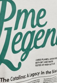 Diseño de texto con "Pme Legends" en hilo verde sobre tela blanca, con texto adicional en negro debajo que habla sobre los aviones de carga y su versatilidad.