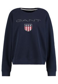 Granatowa bluza wykonana z bawełny, z okrągłym dekoltem, ściągaczami na mankietach oraz przednim logo w kształcie tarczy w kolorach czerwonym, białym i niebieskim.