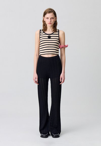Haut court rayé beige et noir avec un accent floral ; associé à un pantalon large noir à côtes présentant une texture en maille.