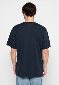 T-shirt in cotone blu navy con maniche corte. Tessuto liscio, scollo a crew, vestibilità casual, con un'etichetta del marchio discreta sul lato.