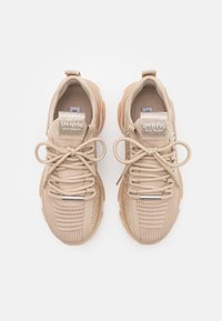 Beige athletic shoes with a textured knit upper, soft laces, and metallic accents on the tongue. Cushioned rubber sole for comfort.