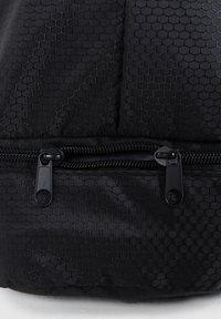 Black backpack featuring a hexagonal textured fabric and dual black zipper pulls, with a contrasting smooth zipper trim.