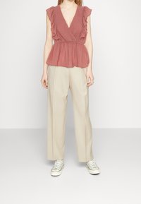 Volang, djup V-ringad, rosafärgad topp med peplummidja, ihop med beige vida byxor och grå sneakers.