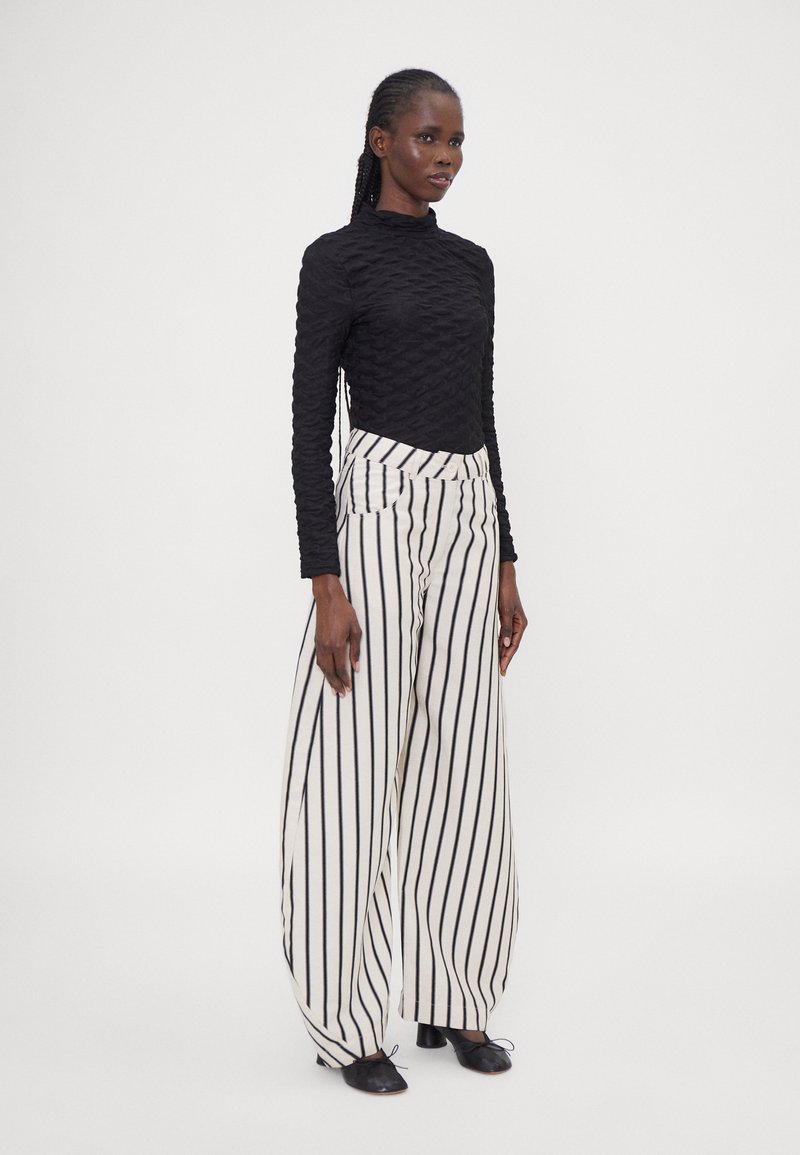 Black textured long-sleeve top paired with high-waisted white and black striped wide-leg pants. Black closed-toe shoes complete the look.