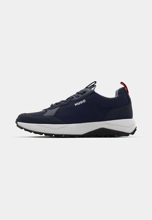 Moške mornarsko modre teniske z zračnim zgornjim delom iz tkanine, kontrastnim sivo midsole, rdečim poudarkom na peti in teksturirano črno gumijasto podplatom.