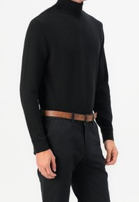 Schwarzer Rollkragenpullover aus weichem Strickstoff, ergänzt durch einen braunen Ledergürtel, getragen mit dunklen Hosen. Schlichtes und tailliertes Design.