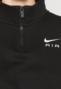 Svart zip-up fleecetröja med hög krage, texturerat tyg och vitt broderat "Nike AIR"-logotyp på bröstet.