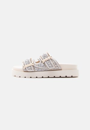 Sandalo beige piatto con due cinturini decorati con perline e strass e fibbie rettangolari in tonalità oro.