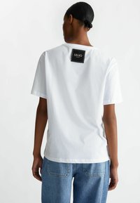 T-shirt bianco in cotone con vestibilità morbida, scollo rotondo e maniche corte. Presenta un'etichetta nera con "LIUJO" sul retro.