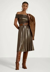 Metalinis bronzinis su one petimi suknelė su diržu juosmenyje, plazdančiu audiniu ir vidutinio ilgio sijonu; derinama su rudomis iki kelių aukštakulnėmis botinėmis ir striuke.