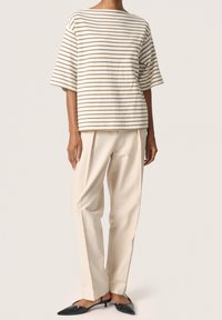 Gestreiftes kurzärmliges Oberteil in Off-White und Hellbraun, kombiniert mit beigen, gefalteten Hosen und schwarzen spitzen Schuhen.