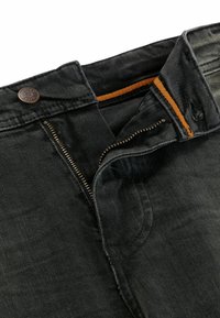 Black denim jeans with a zip fly and orange stitching. Features a brass button and a textured fabric for durability.