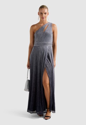Donna che indossa un elegante abito argento scintillante a spalla scoperta con uno spacco laterale alto fino alla coscia, tiene una piccola borsa argentata ed indossa sandali neri.