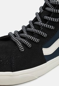 Sapatilha alta em camurça preta com faixa lateral texturizada branca, painel de malha azul e atacadores trançados em preto e branco. Sola de borracha.
