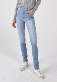 Jeans ajustados de color azul claro, fabricados en denim, con una cintura de altura media, bolsillos delanteros y un acabado limpio. Combinados con zapatillas blancas.