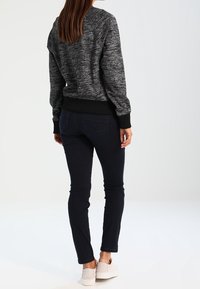 Zwarte en grijze gebreide trui met geribde manchetten, gecombineerd met donkerblauwe slim-fit jeans en lichtgekleurde sneakers, gezien vanuit de achterkant.