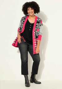 Cárdigan colorido con acentos rosas, patrones en negro y gris, llevado sobre una camiseta negra. Complementado con vaqueros oscuros y botines negros con tachuelas.